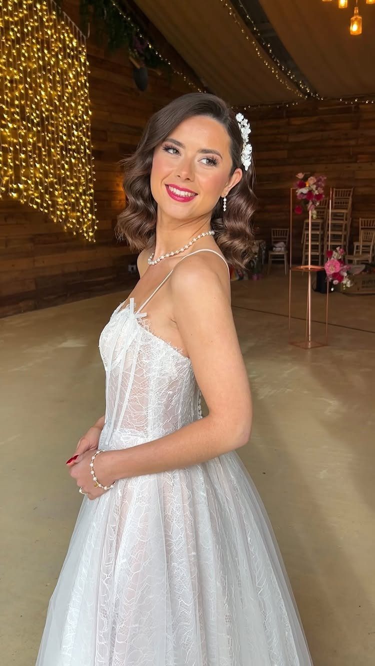 A woman with wavy short hair and a floral accessory wearing a white lace wedding dress.