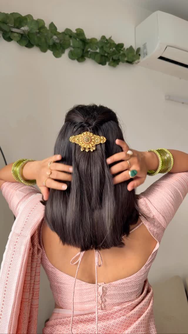 Woman with short black hair styled with a large gold hair clip and pink saree.
