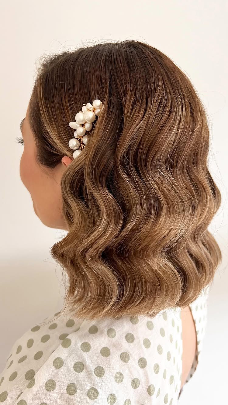 Woman with wavy brown hair adorned with a pearl hair clip.