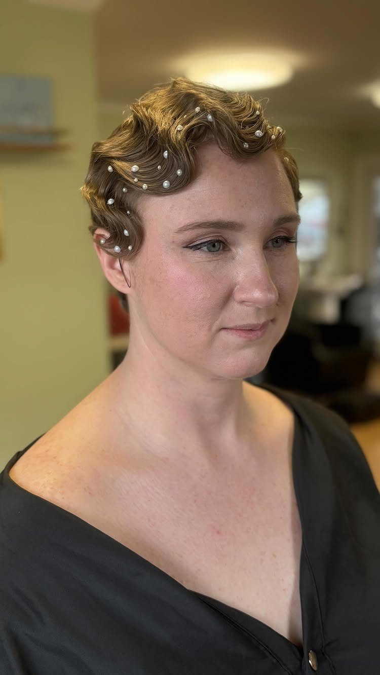 Person with short wavy hair decorated with small white pearls and styled in finger waves.