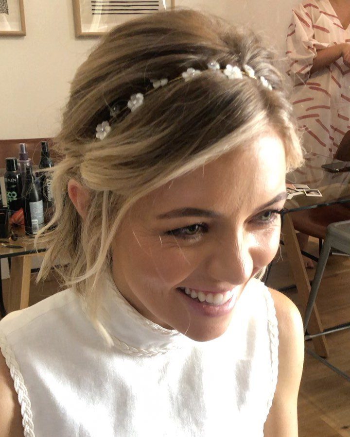 Smiling woman with blonde short hair wearing a white floral headband and a white top.