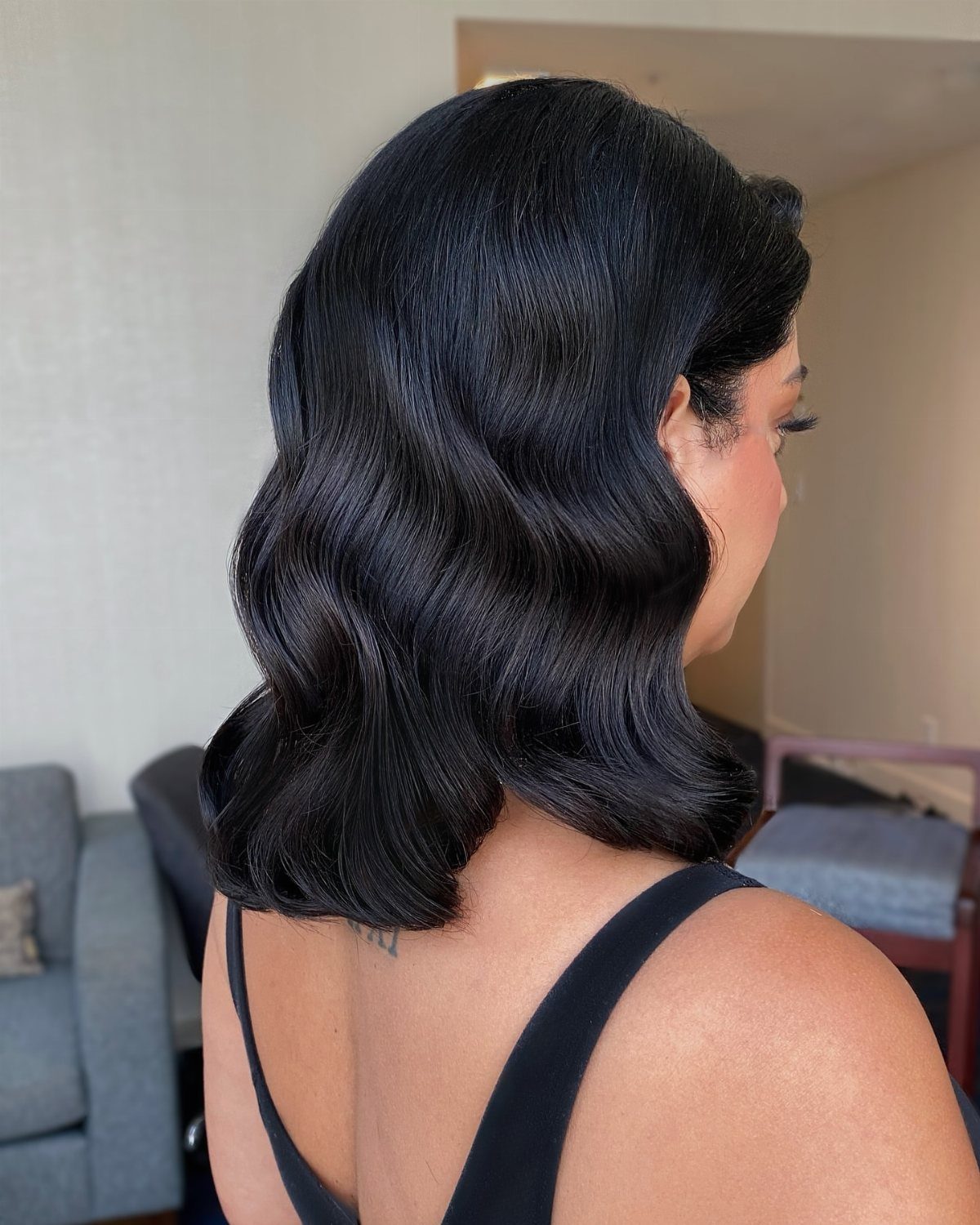 Woman with dark hair styled in glamorous, structured Hollywood waves seen from the side.