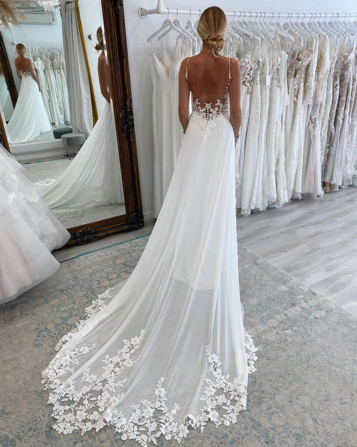 Woman wearing a white backless A-line wedding gown with floral lace train in bridal shop