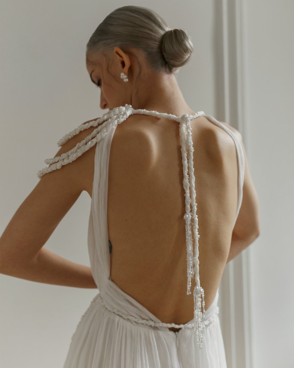 Woman from behind wearing a white backless wedding dress with beaded straps.