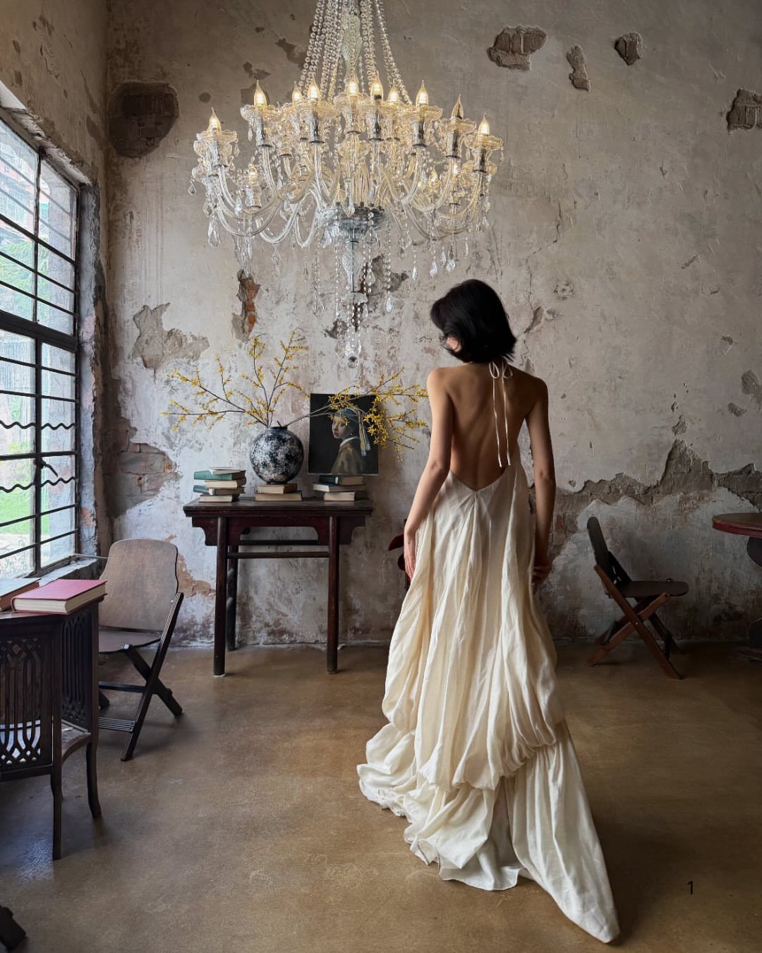 Woman in a cream silk backless gown standing in a rustic room with chandelier