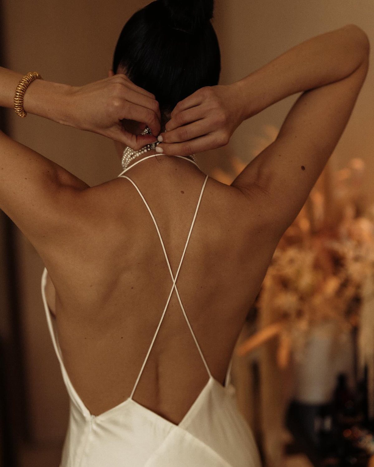 Woman wearing a white silk backless gown with thin crisscross straps from behind.