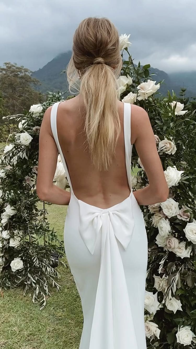 Woman in a backless white silk wedding dress with a bow at the back.