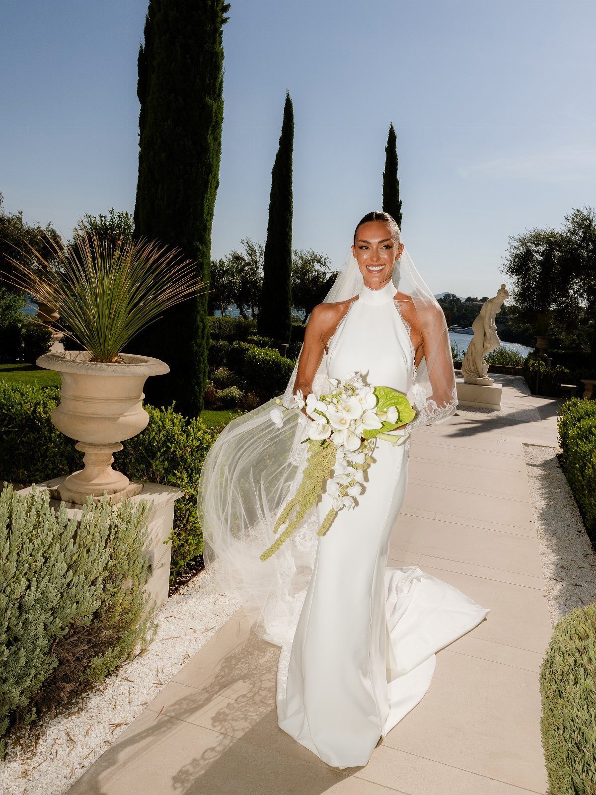 Woman in a white silk halter-neck wedding dress holding a bouquet in a garden