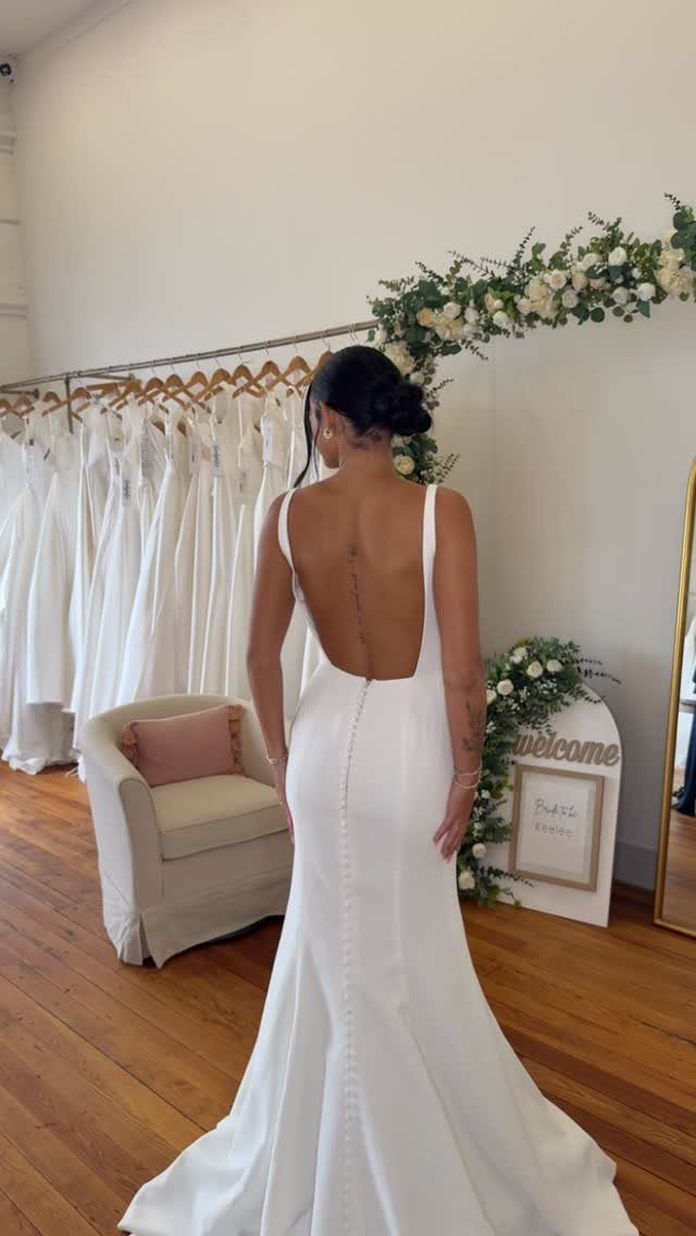 Woman wearing a white wedding dress with a deep square open back and buttons.