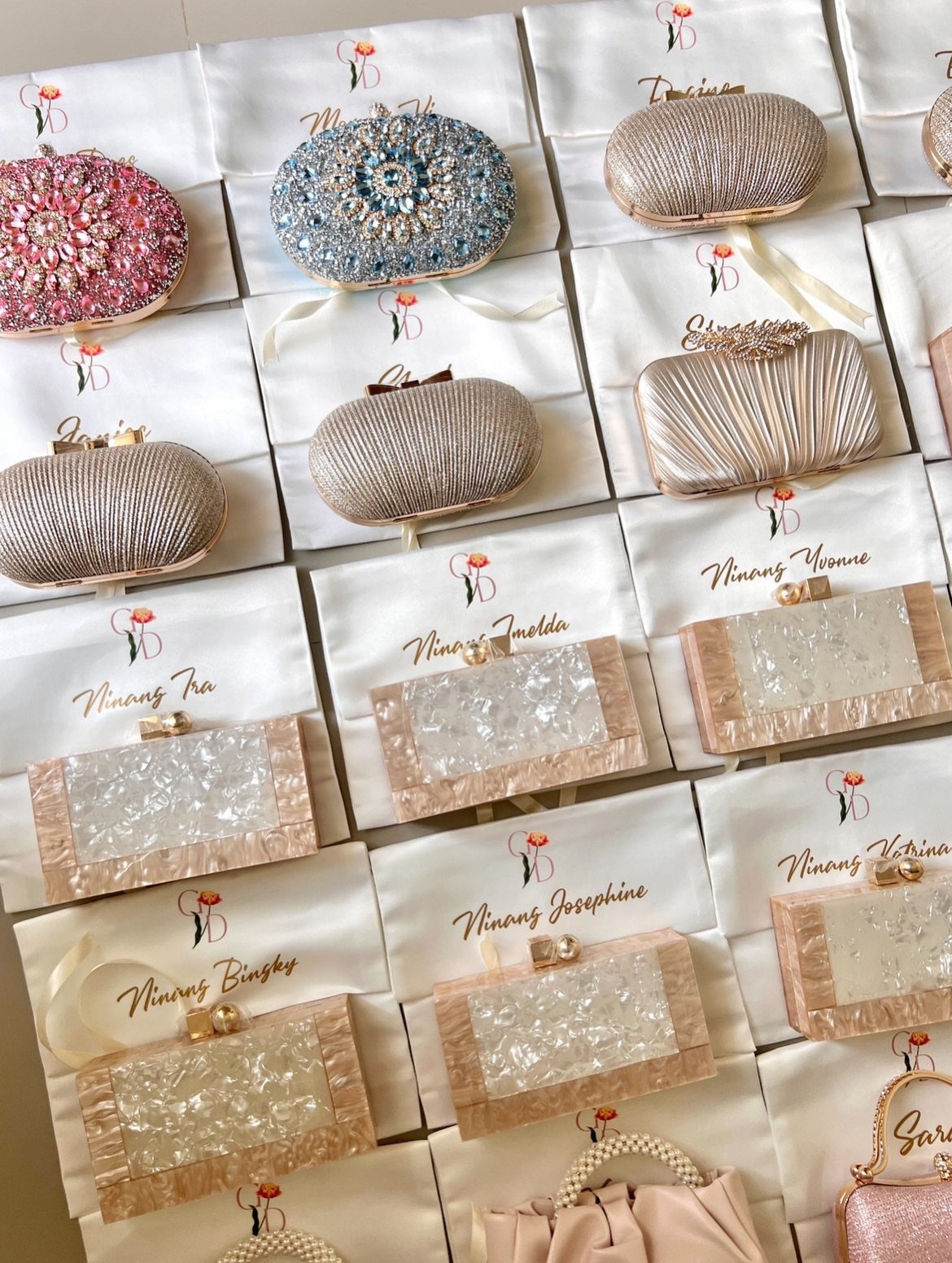 Sister Wedding Gift Ideas: 34 Picks She'll Treasure 10 Assorted formal clutch purses resting on personalized white fabric bags with names.