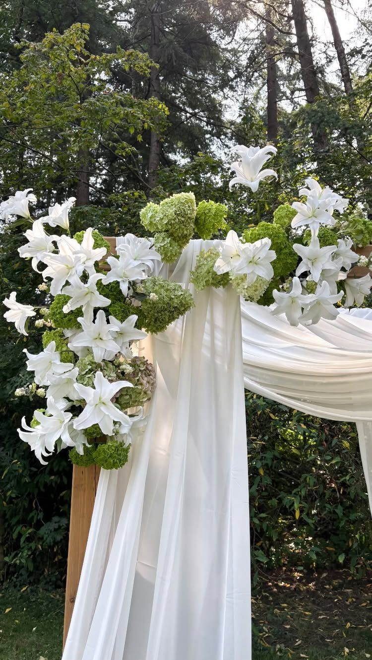 White floral wedding arch with lilies and fabric in a green garden setting