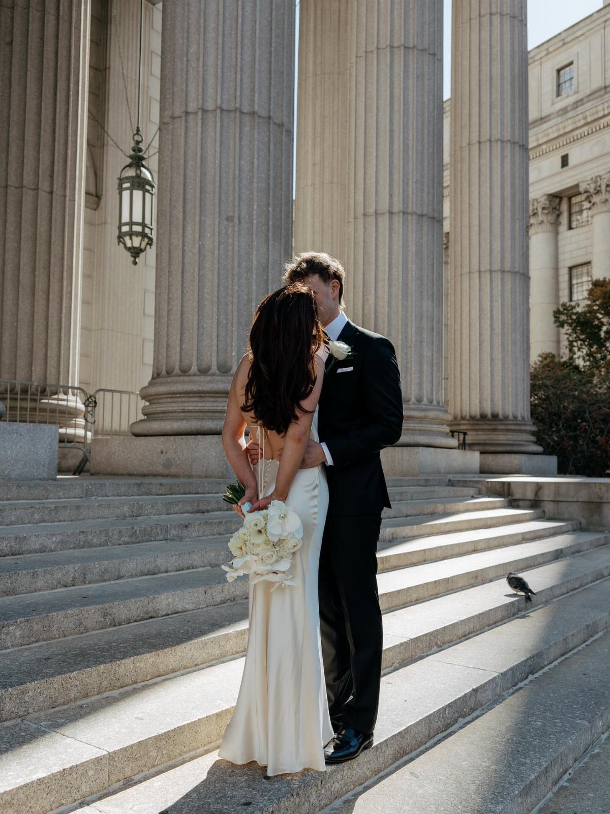 Bride and groom embracing on stone steps in front of classical columns.