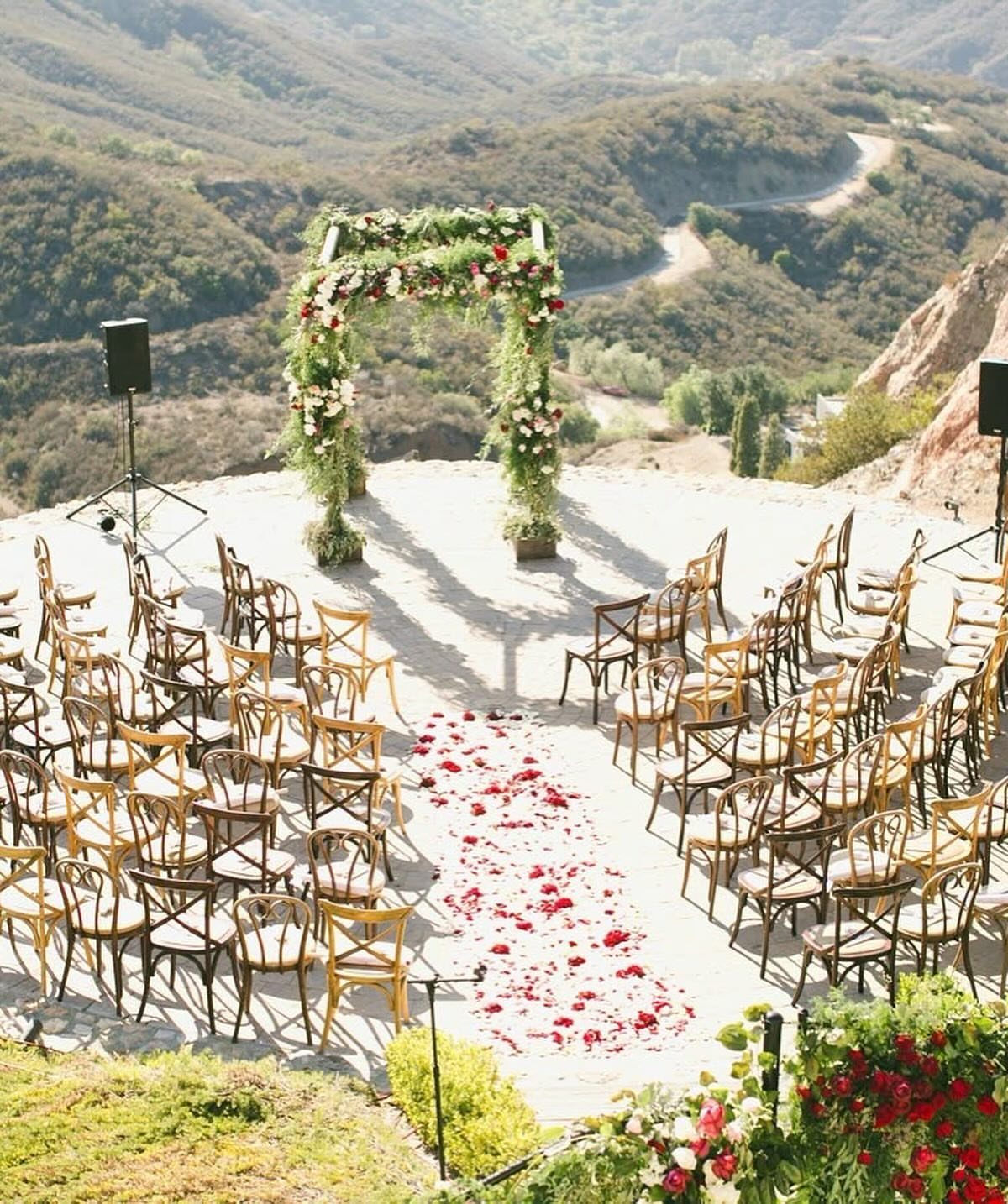 Curved rows of wooden chairs facing a floral arch on a mountain overlook.