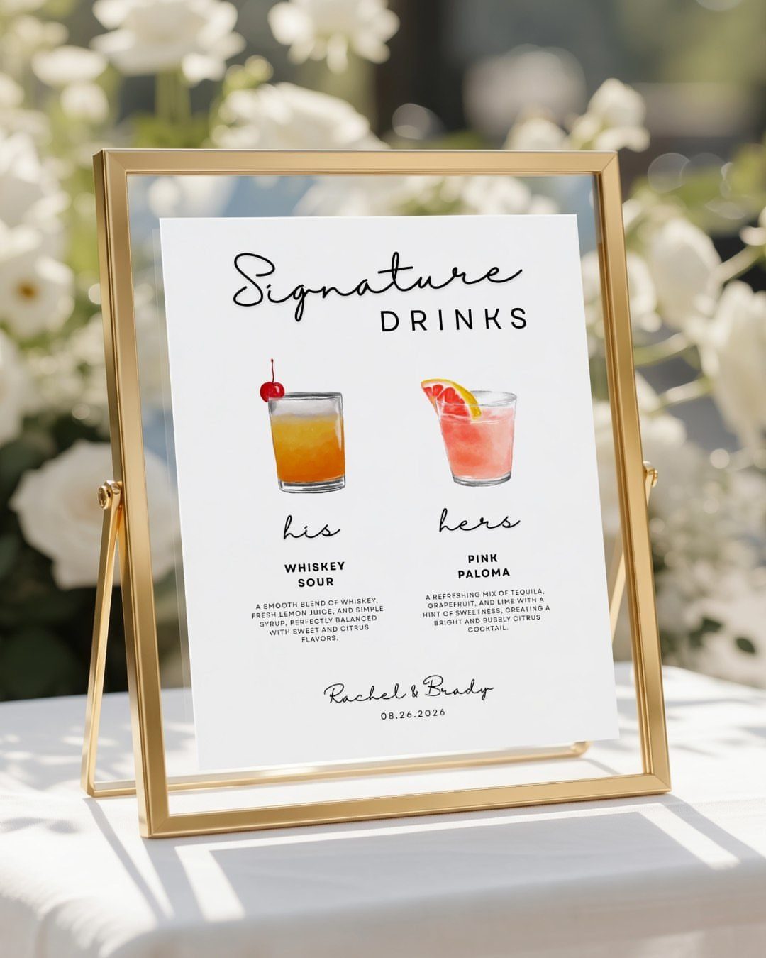 Gold-framed signature drinks sign with cocktail illustrations on a white wedding table.