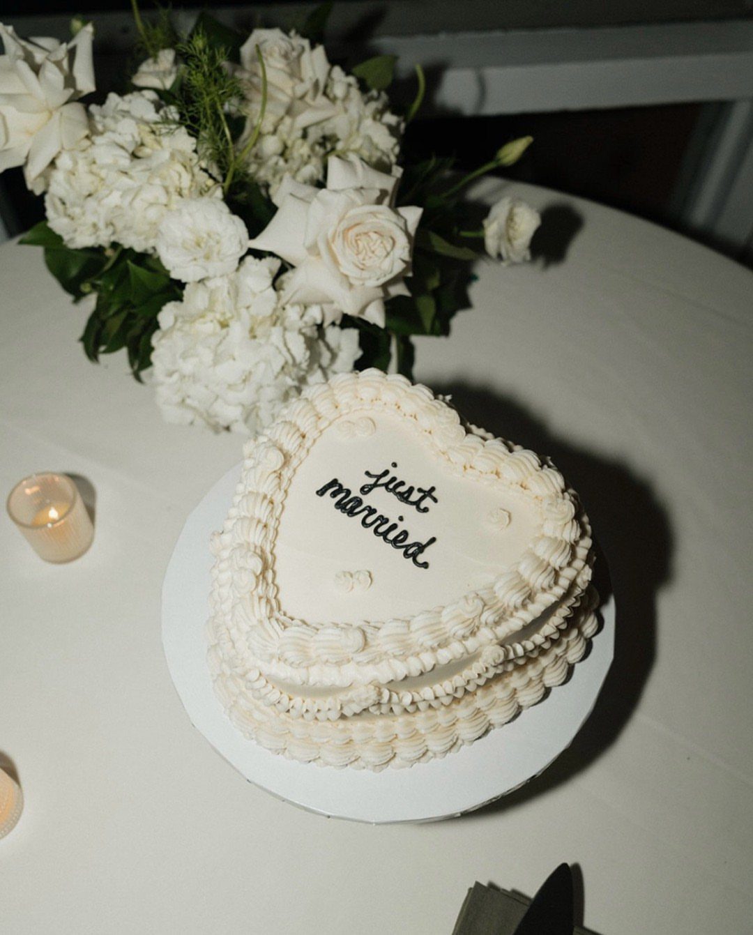 Heart-shaped white wedding cake with just married text and white floral bouquet.