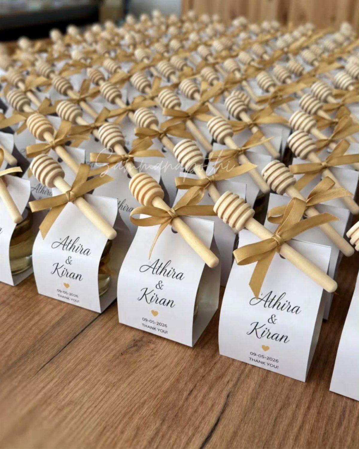 20 Small Wedding Gift Ideas for Couples Who Have Everything 11 Small honey jars with white personalized labels, gold ribbons, and wooden honey dippers.