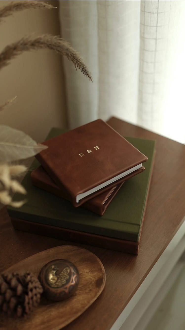 20 Small Wedding Gift Ideas for Couples Who Have Everything 19 Brown leather journal with gold initials D & H resting on a stack of books.