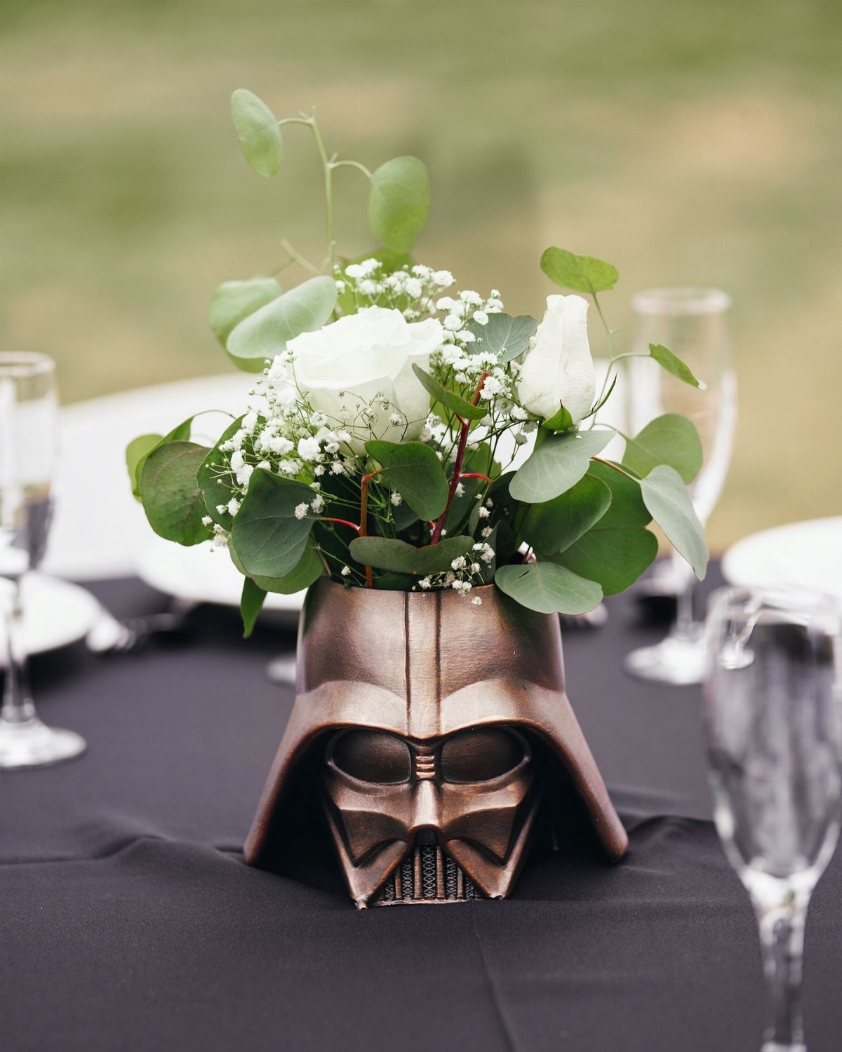 Darth Vader helmet vase with white roses and greenery on a black table