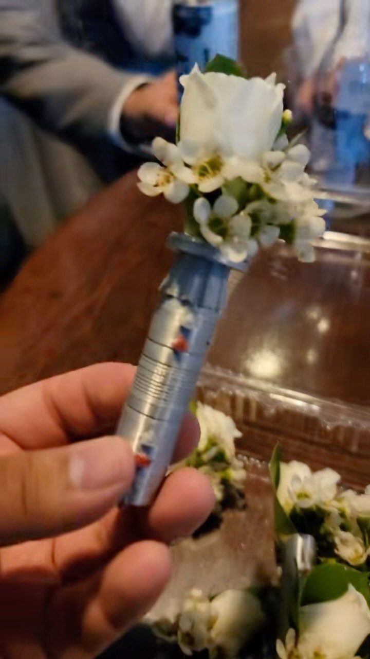 Lightsaber hilt topped with white roses and baby's breath as a wedding boutonniere.