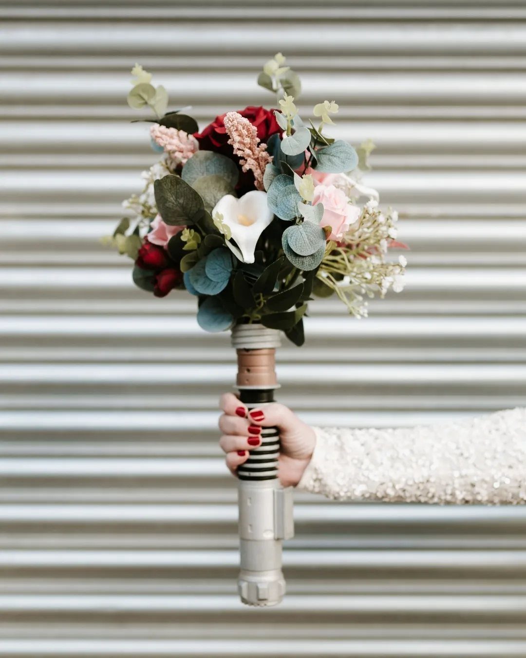 Wedding bouquet of red and white flowers with a lightsaber hilt as the handle