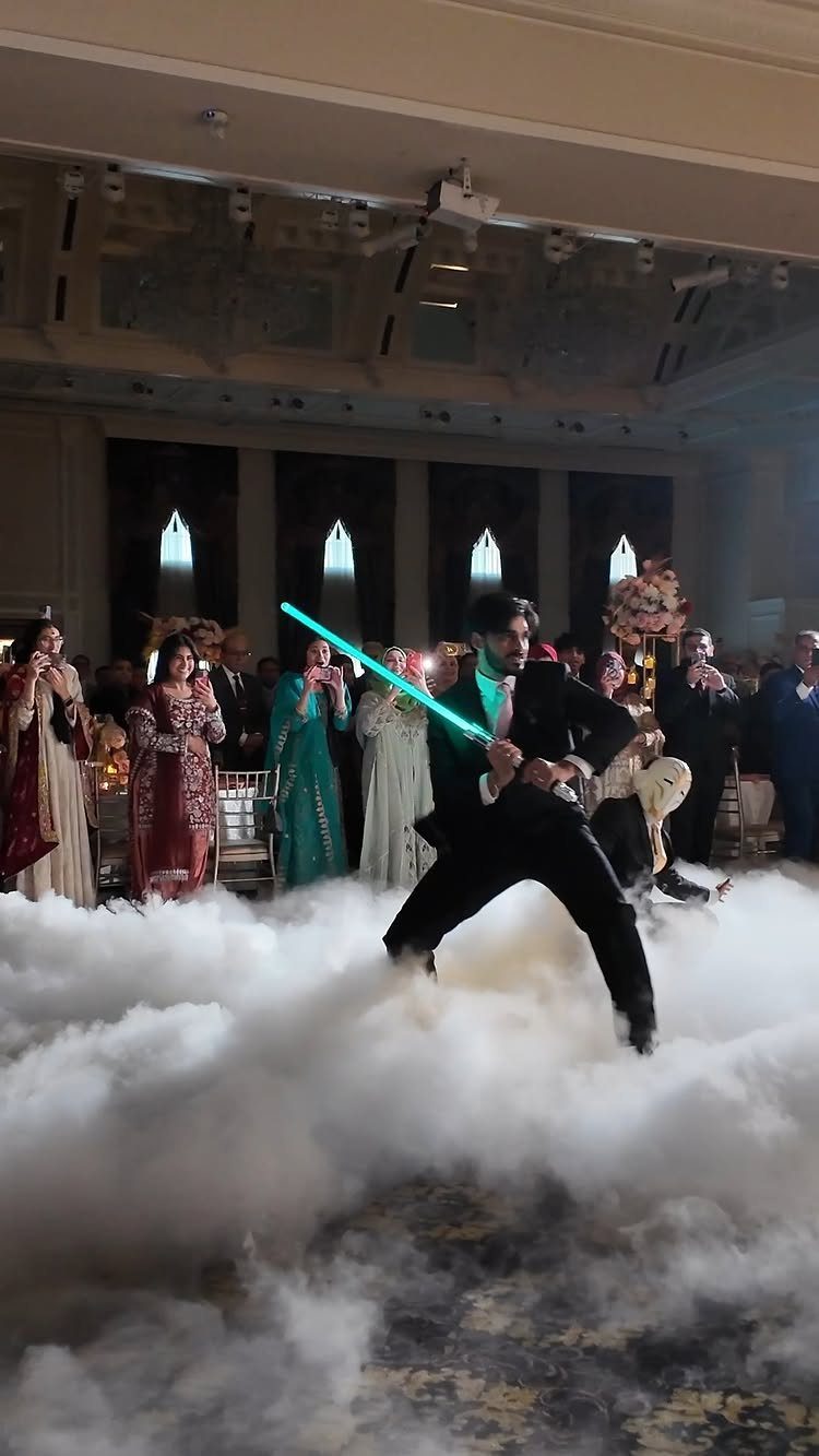 Man in a suit wielding a blue lightsaber amidst white fog at a wedding.