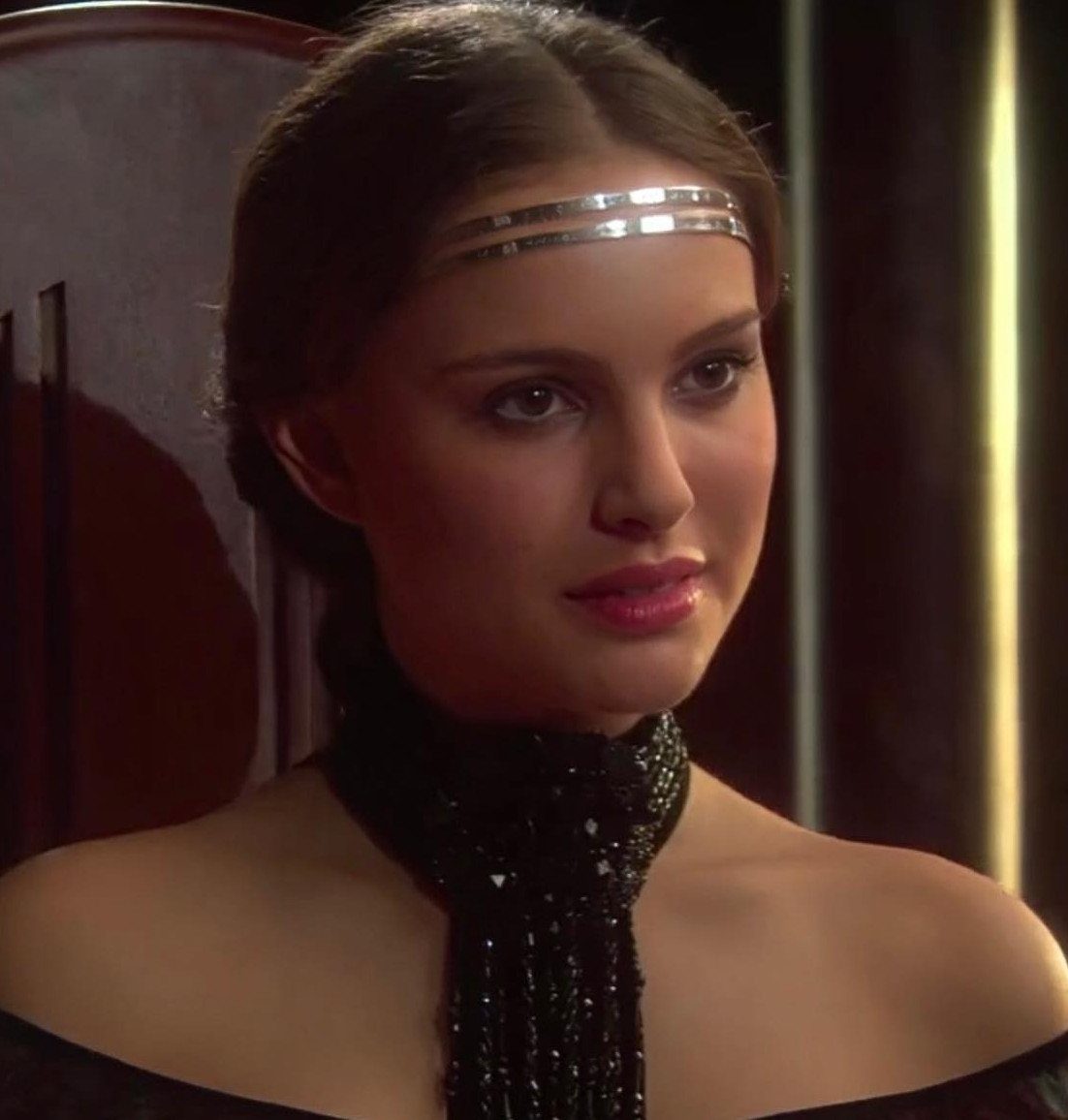Woman with an elegant updo and silver headband wearing a black beaded collar.