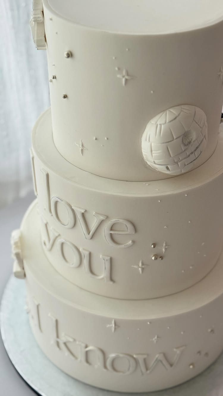 Three-tiered white wedding cake with a Death Star and Star Wars quotes.