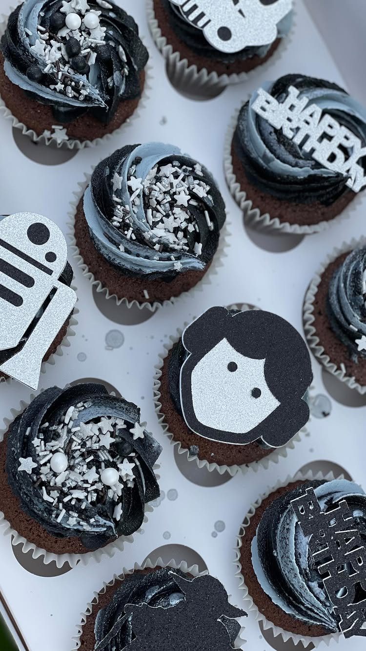 Chocolate cupcakes with black frosting and Star Wars character cutouts and silver stars.