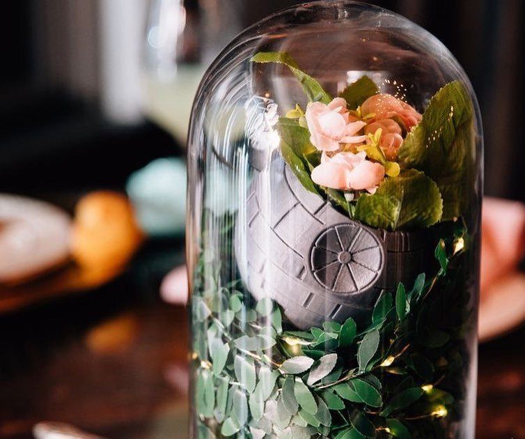 Death Star model with pink flowers and greenery inside a glass cloche centerpiece