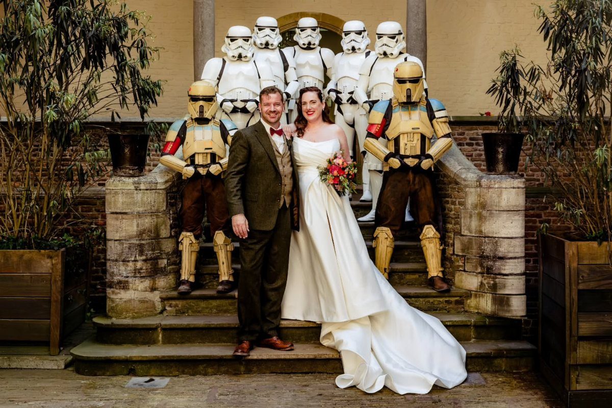 Bride and groom posing on stone steps surrounded by Stormtroopers and Scout Troopers.