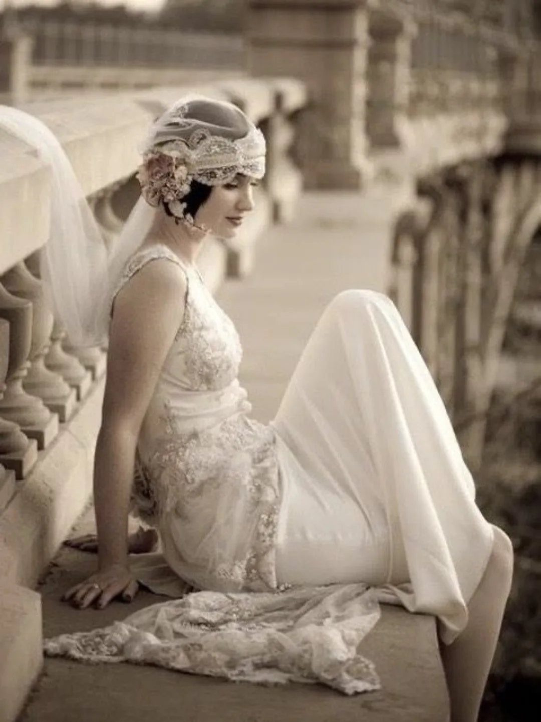 Vintage Elegant Wedding Dress Ideas in 12 Styles 2 Woman in a 1920s-inspired wedding dress and cloche veil sitting on stone railing.