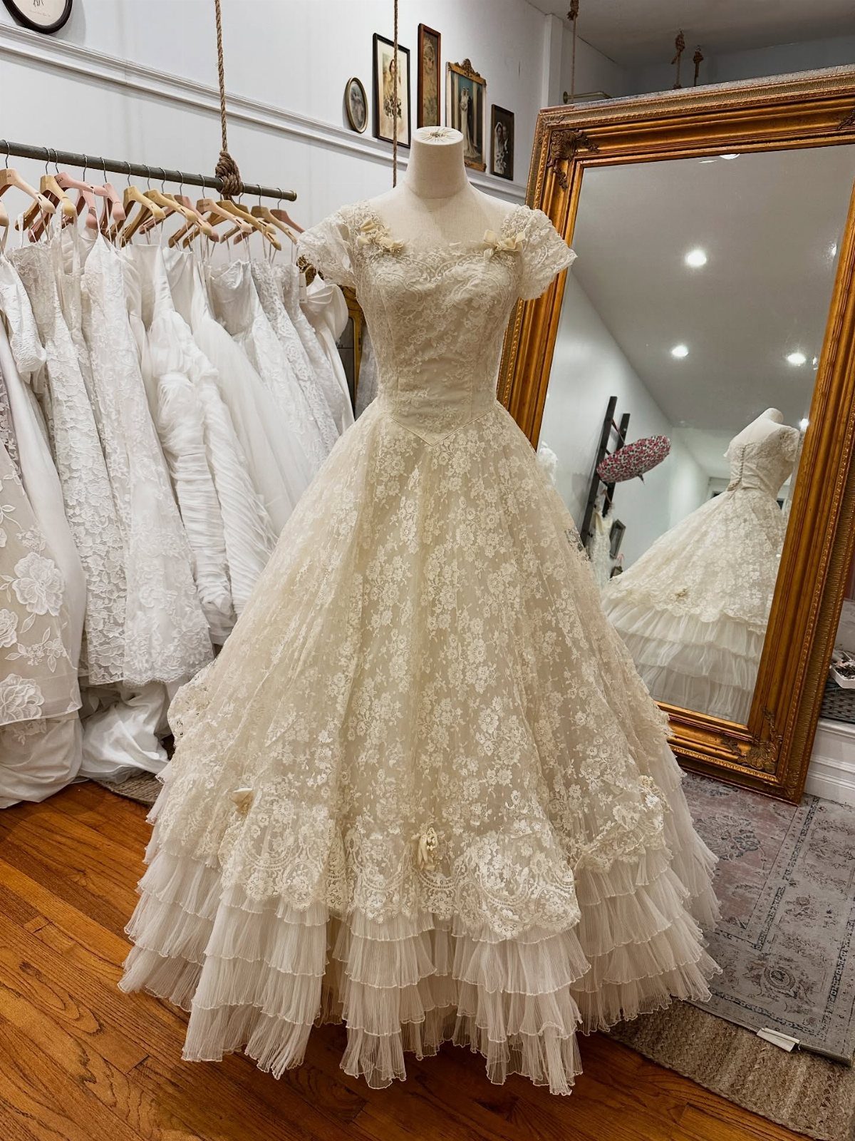Vintage Elegant Wedding Dress Ideas in 12 Styles 4 Vintage lace wedding dress on a mannequin inside a bridal boutique with gold mirror.