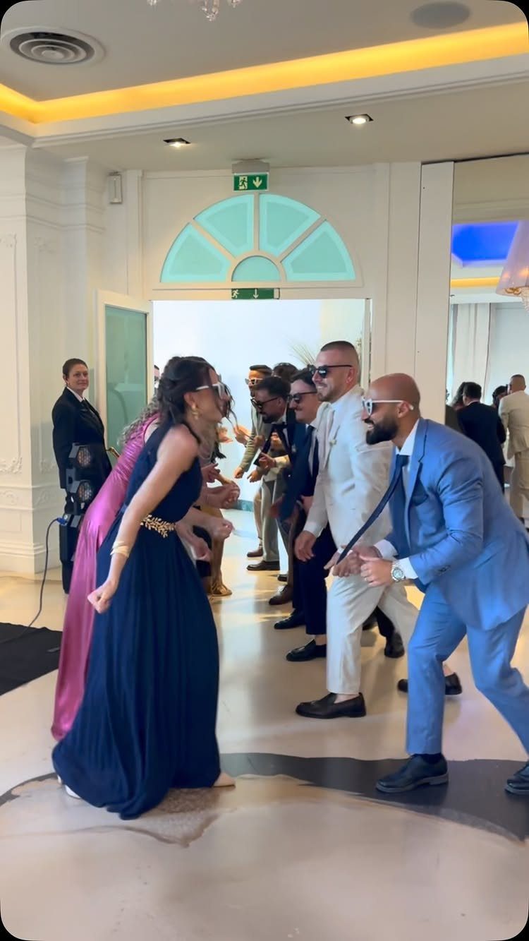 19 Wedding Activities for Guests: Reception Ideas Fun Enough to Fill the Whole Night 7 People in formal wedding attire dancing energetically together in a bright, modern reception hall.