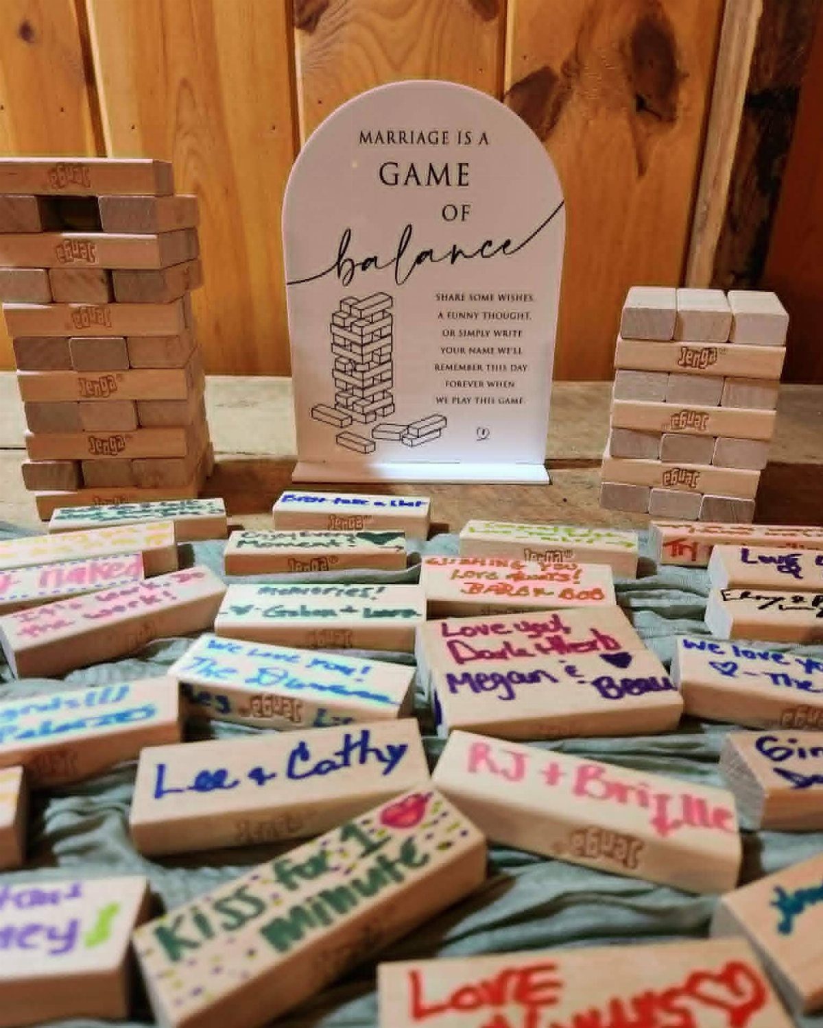 19 Wedding Activities for Guests: Reception Ideas Fun Enough to Fill the Whole Night 14 Wooden Jenga blocks with handwritten wedding messages scattered on a blue cloth near a decorative sign.