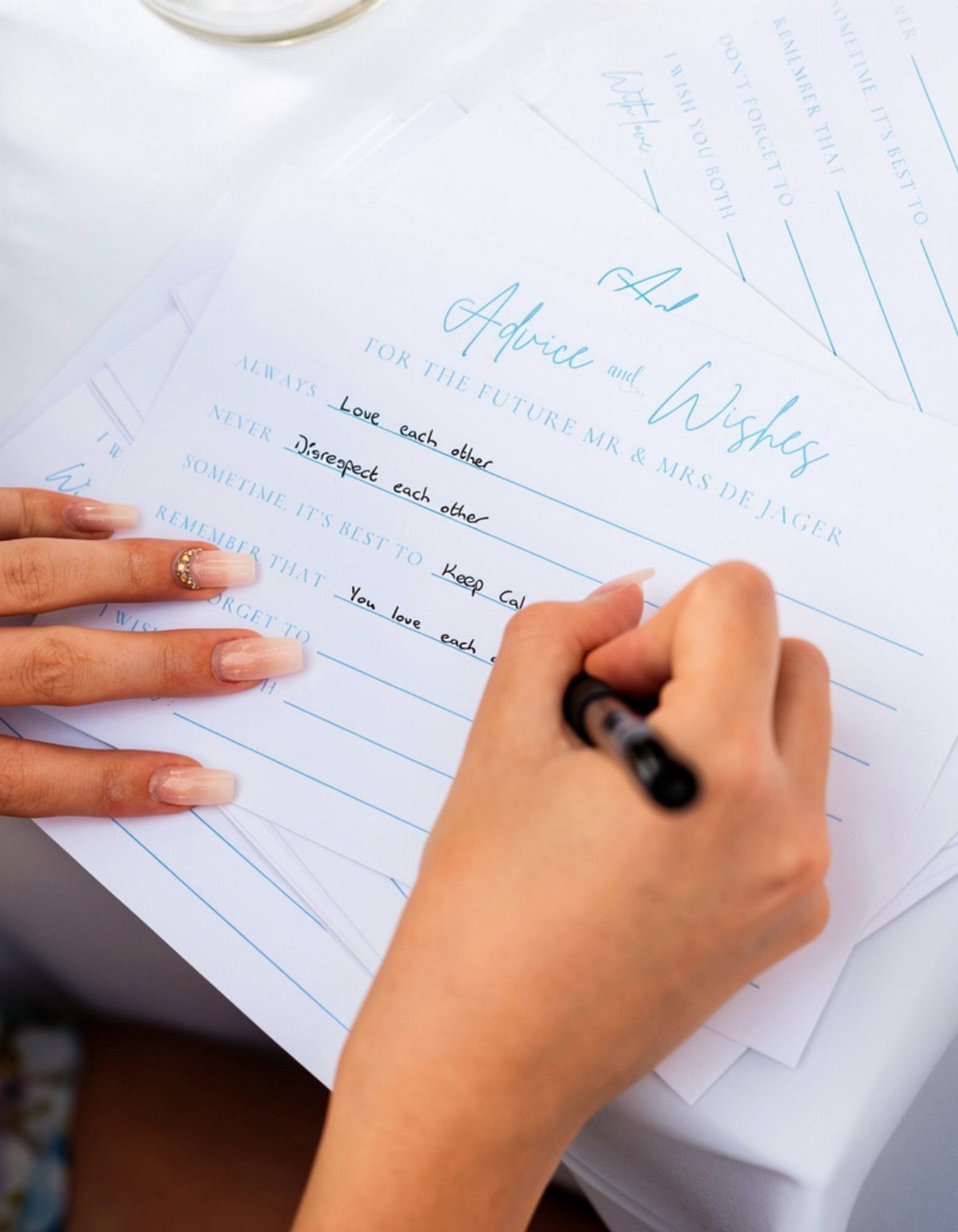 19 Wedding Activities for Guests: Reception Ideas Fun Enough to Fill the Whole Night 11 Hands writing marriage advice on a white card with blue text and lines.