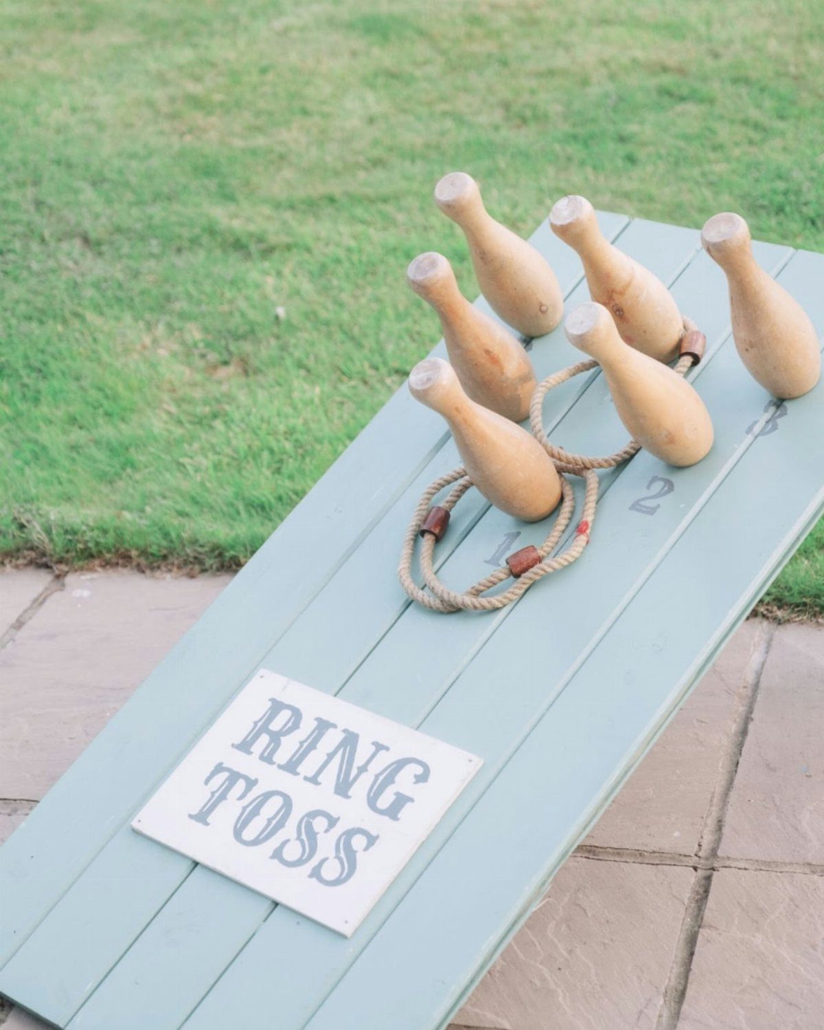 19 Wedding Activities for Guests: Reception Ideas Fun Enough to Fill the Whole Night 8 Wooden ring toss pins and rope rings resting on a light blue wooden board outdoors.
