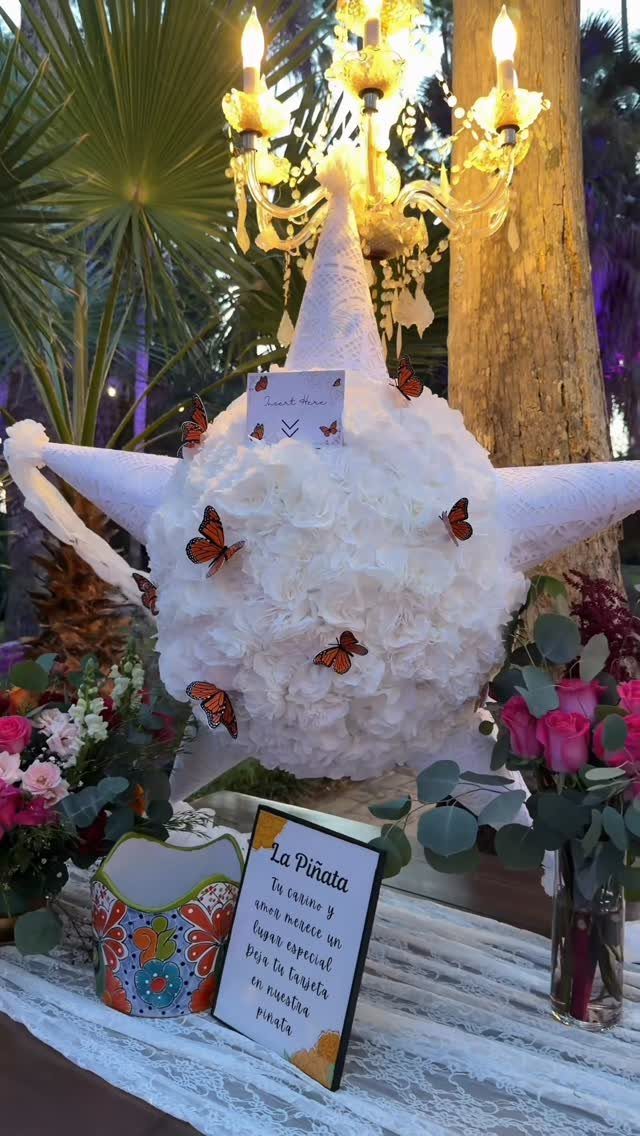 19 Wedding Activities for Guests: Reception Ideas Fun Enough to Fill the Whole Night 17 A white decorative piñata adorned with orange butterflies sits on a table with flowers and a sign.