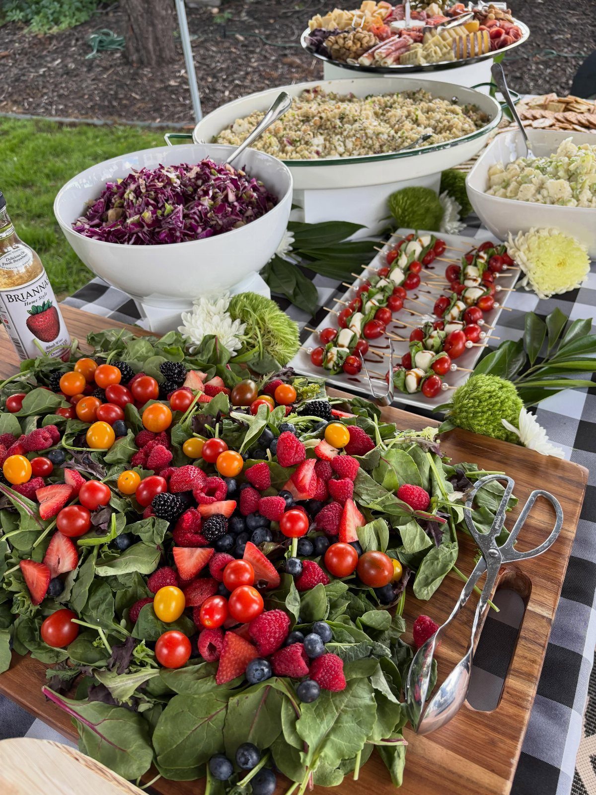 35 Backyard Wedding Reception Ideas for an Unforgettable Day 32 Buffet spread with berry salad, coleslaw, and caprese skewers on a checkered tablecloth.