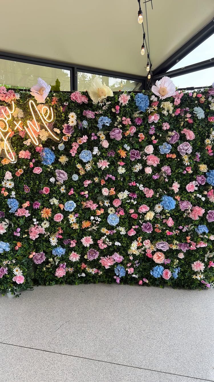 35 Backyard Wedding Reception Ideas for an Unforgettable Day 9 Floral wall with pink and blue flowers and a neon sign on greenery.