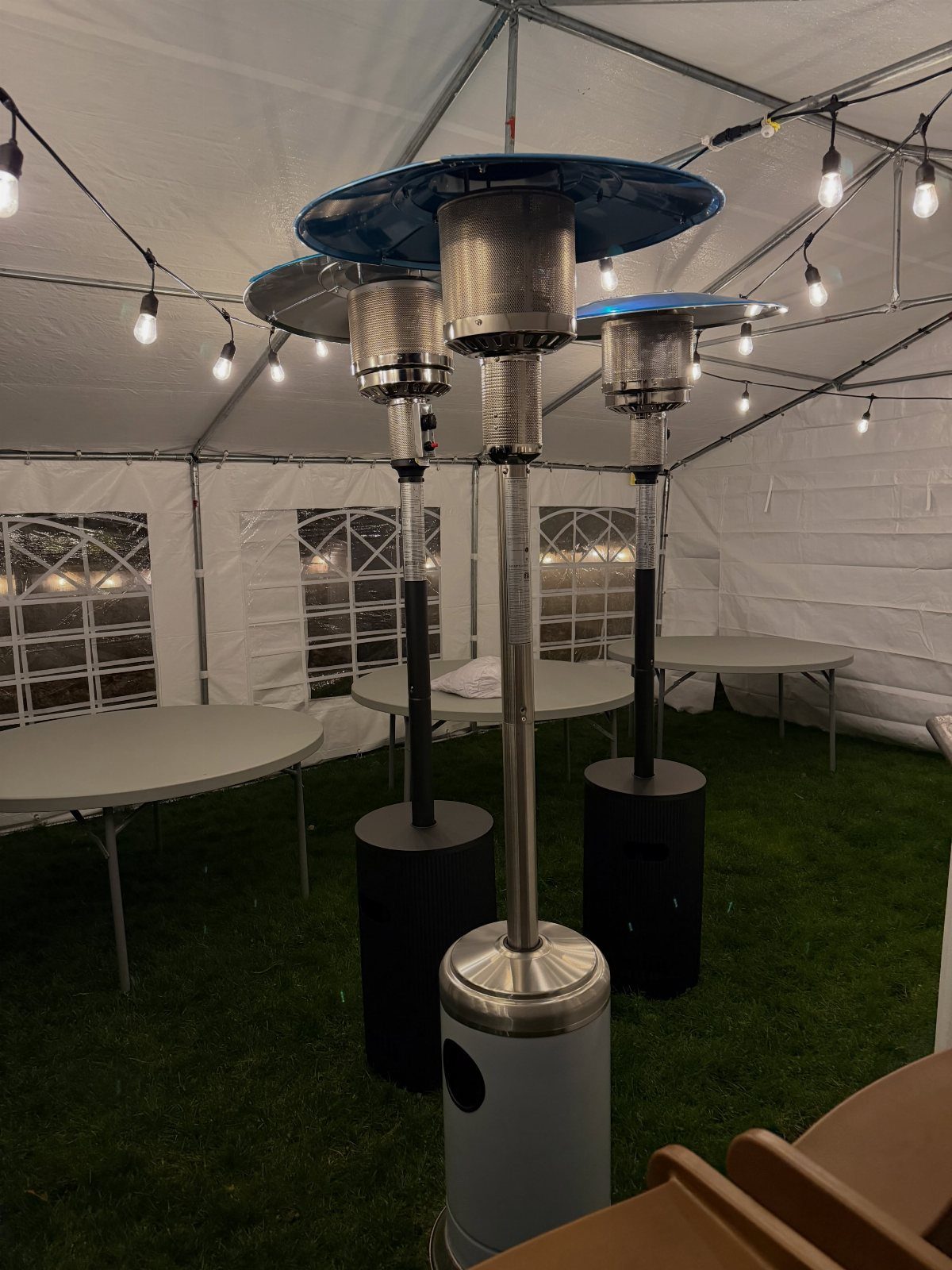 35 Backyard Wedding Reception Ideas for an Unforgettable Day 29 Three tall silver patio heaters with blue tops inside a white wedding tent.