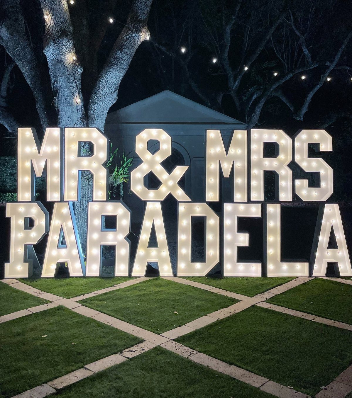 35 Backyard Wedding Reception Ideas for an Unforgettable Day 27 Large white light-up marquee letters spelling MR & MRS PARADELA on a green lawn