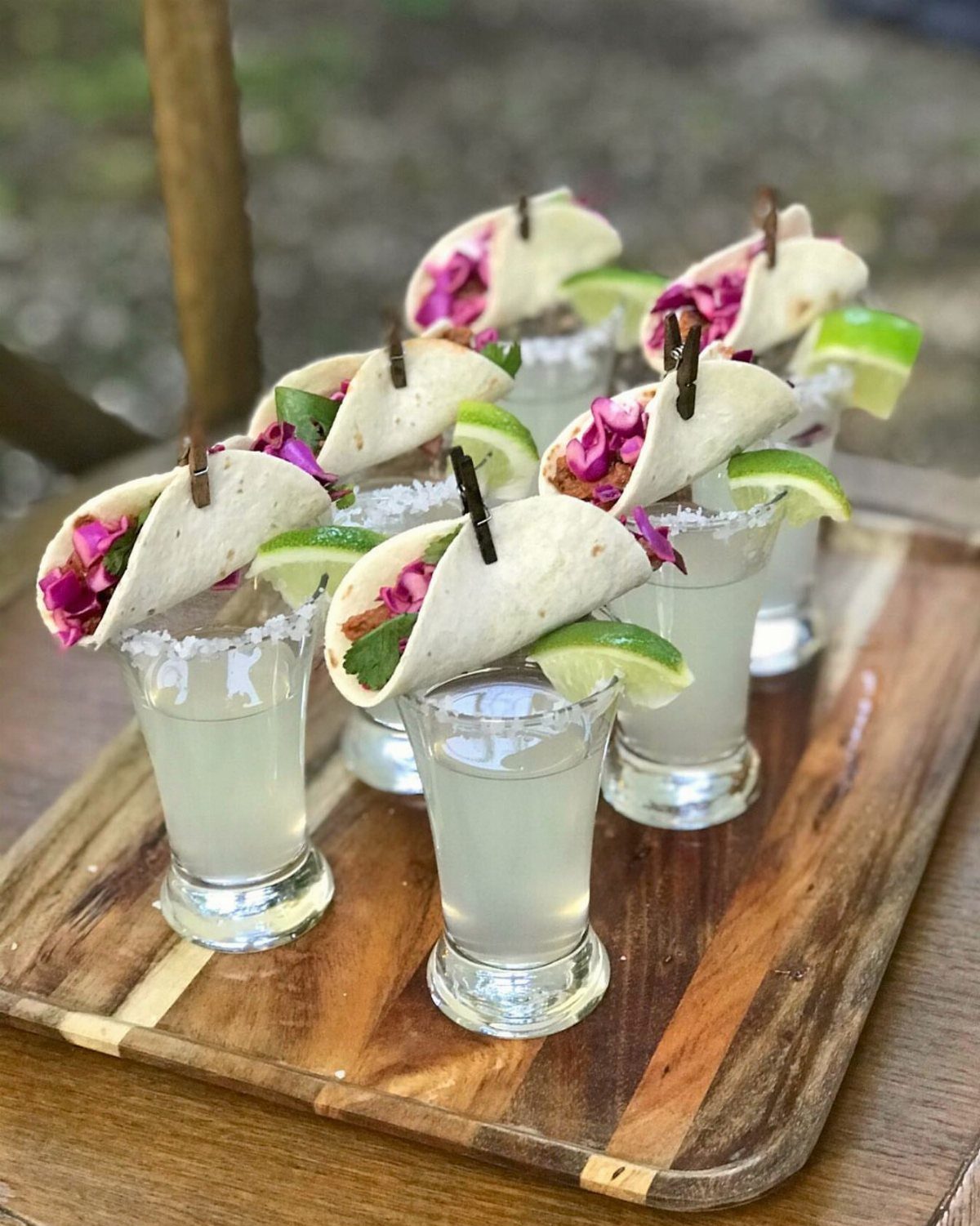 35 Backyard Wedding Reception Ideas for an Unforgettable Day 34 Mini tacos balanced on shot glasses with lime wedges on a wooden tray.