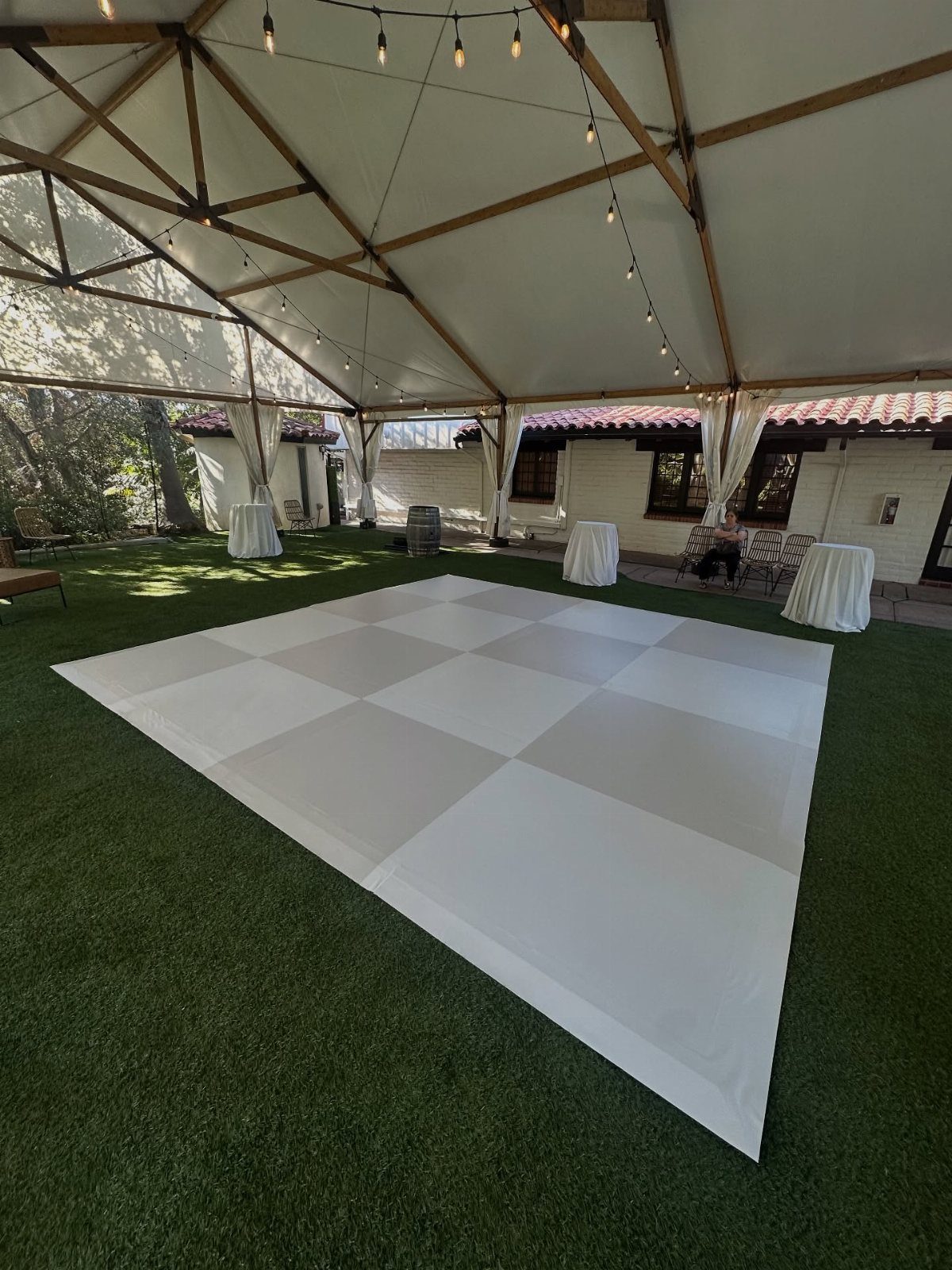 35 Backyard Wedding Reception Ideas for an Unforgettable Day 17 White checkered dance floor on green grass under a white event tent with lights.