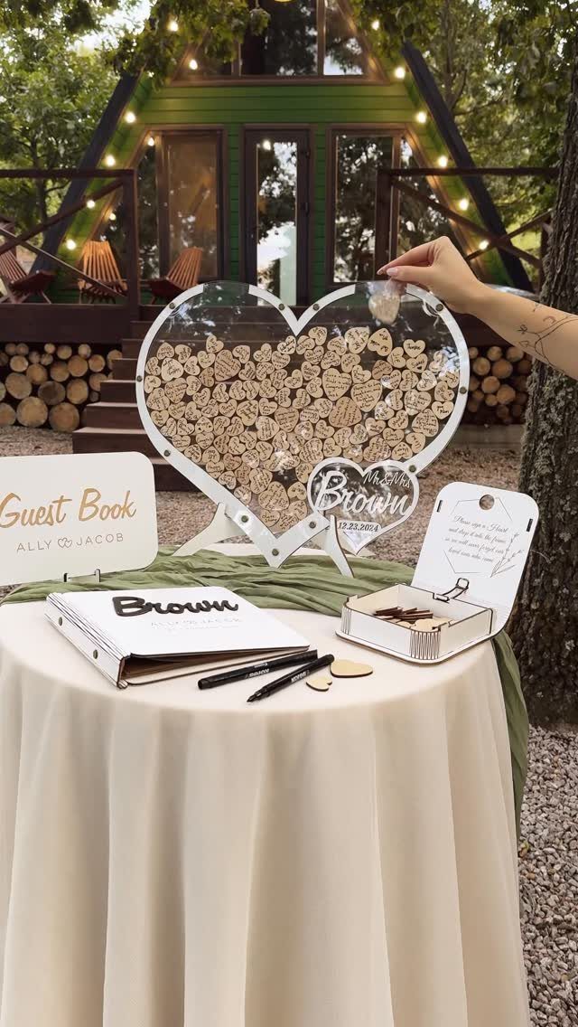 35 Backyard Wedding Reception Ideas for an Unforgettable Day 5 Heart-shaped acrylic guest book frame with wooden tokens on a white tablecloth.