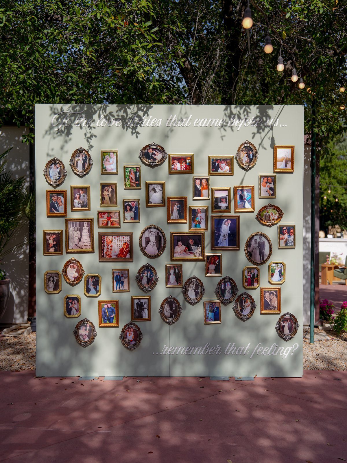 35 Backyard Wedding Reception Ideas for an Unforgettable Day 25 Wall of framed couple photographs displayed as outdoor wedding reception decor under a tree.