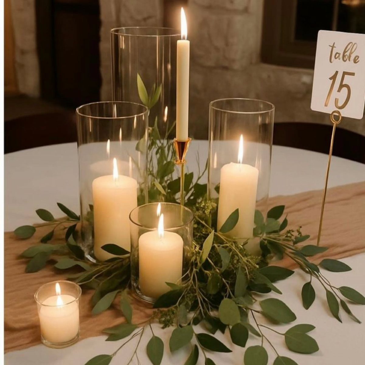 35 Backyard Wedding Reception Ideas for an Unforgettable Day 26 White candles in glass cylinders with eucalyptus greenery on a tan table runner.