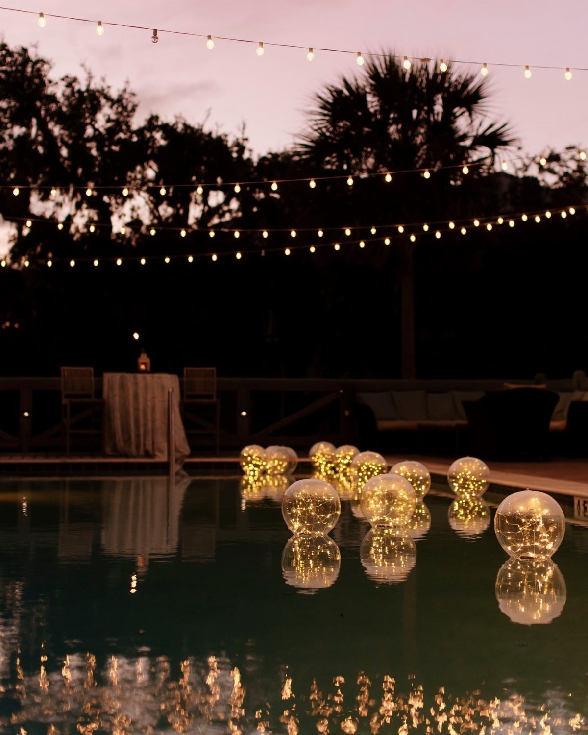 35 Backyard Wedding Reception Ideas for an Unforgettable Day 2 Glowing spherical lights floating in a swimming pool under overhead string lights at dusk.
