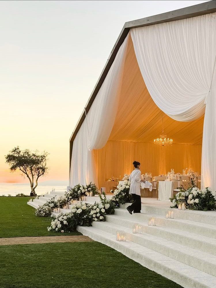 35 Backyard Wedding Reception Ideas for an Unforgettable Day 3 Large white wedding tent with draped fabric, floral arrangements, and white carpeted steps.