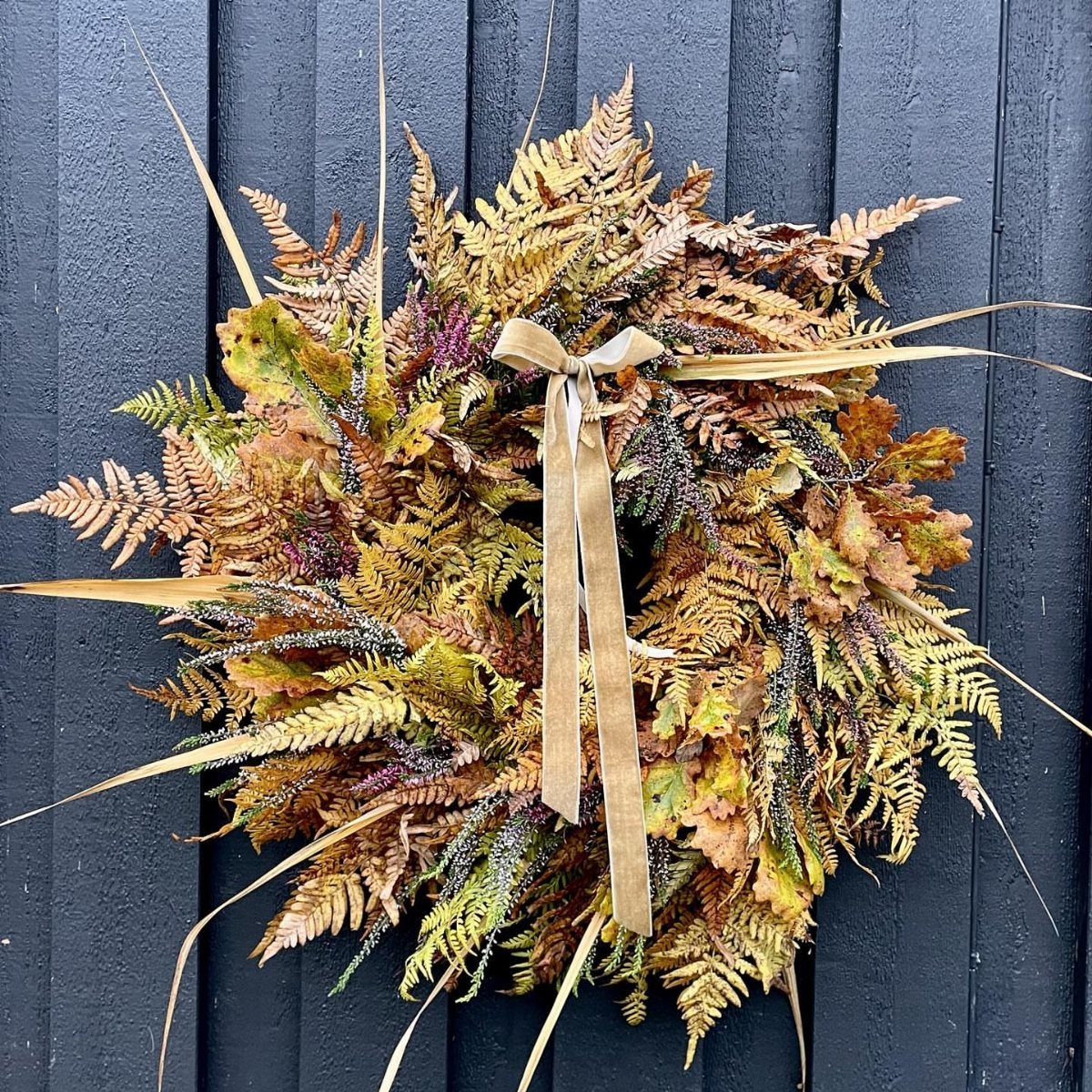 12 Wedding Bouquet Alternatives for Your Big Day 10 Dried fern leaf wreath with a tan ribbon bow on a dark wall.