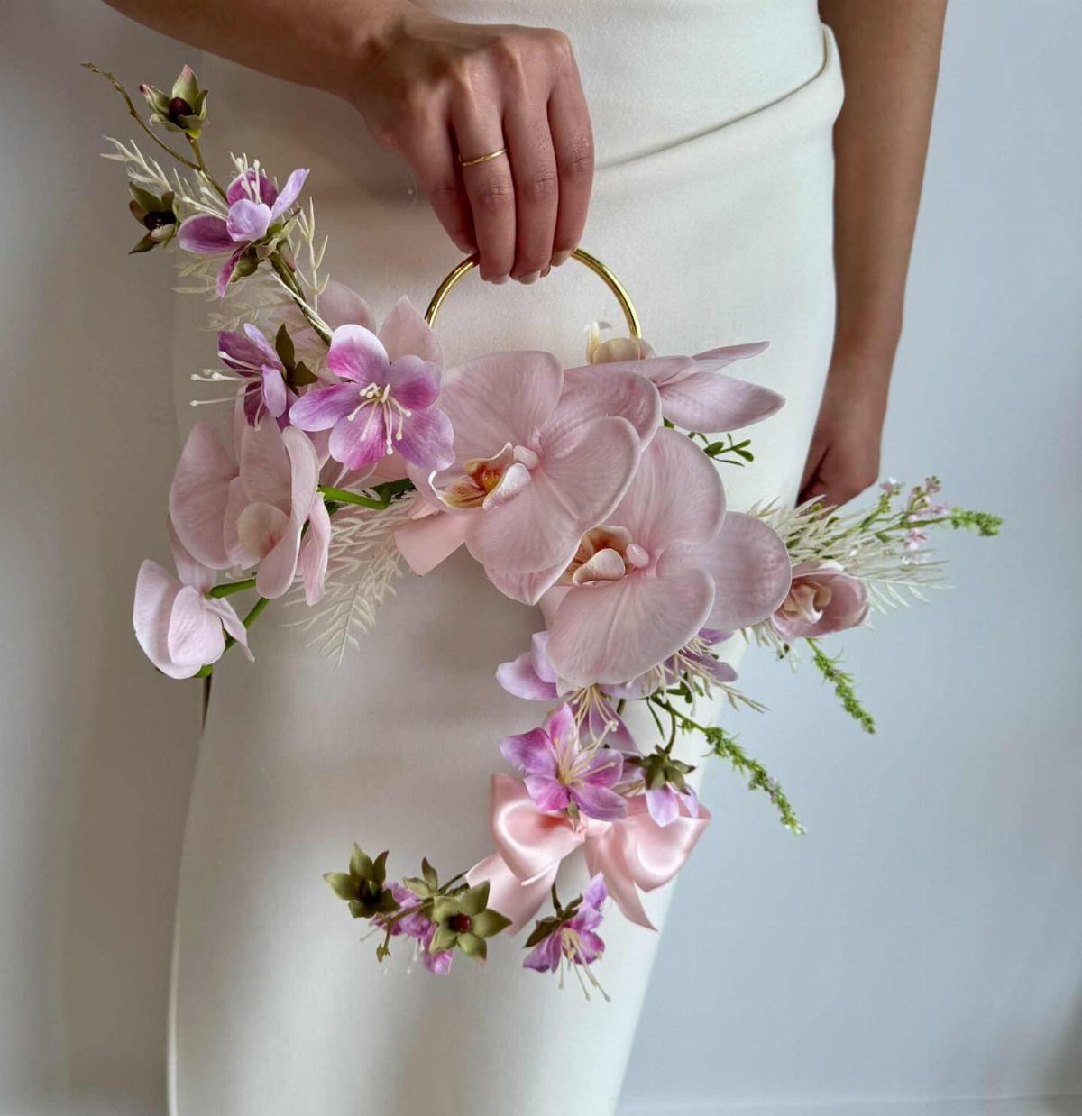12 Wedding Bouquet Alternatives for Your Big Day 6 Gold floral hoop with pink orchids and greenery held by a person in white.